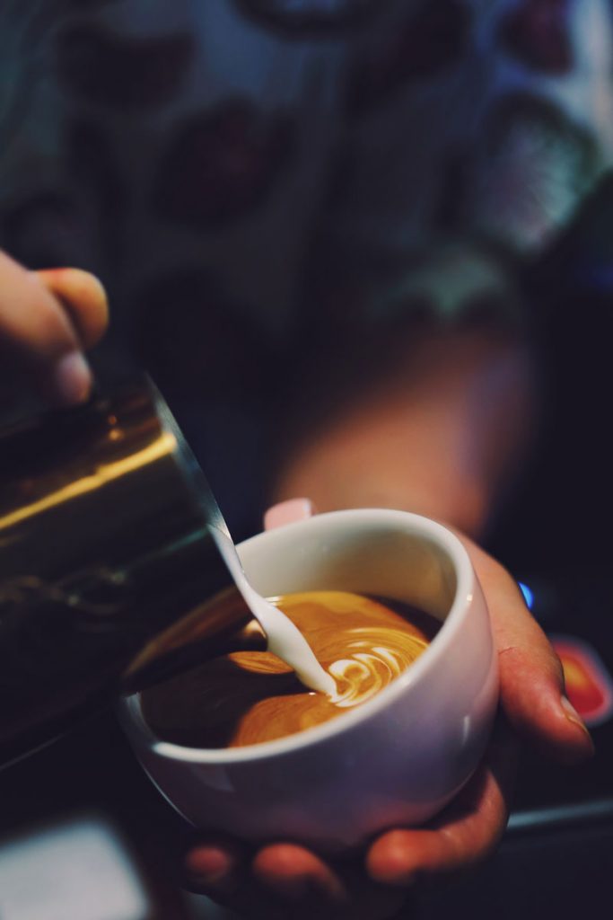 Mann hält eine Kaffeetasse und gießt Milch ein
